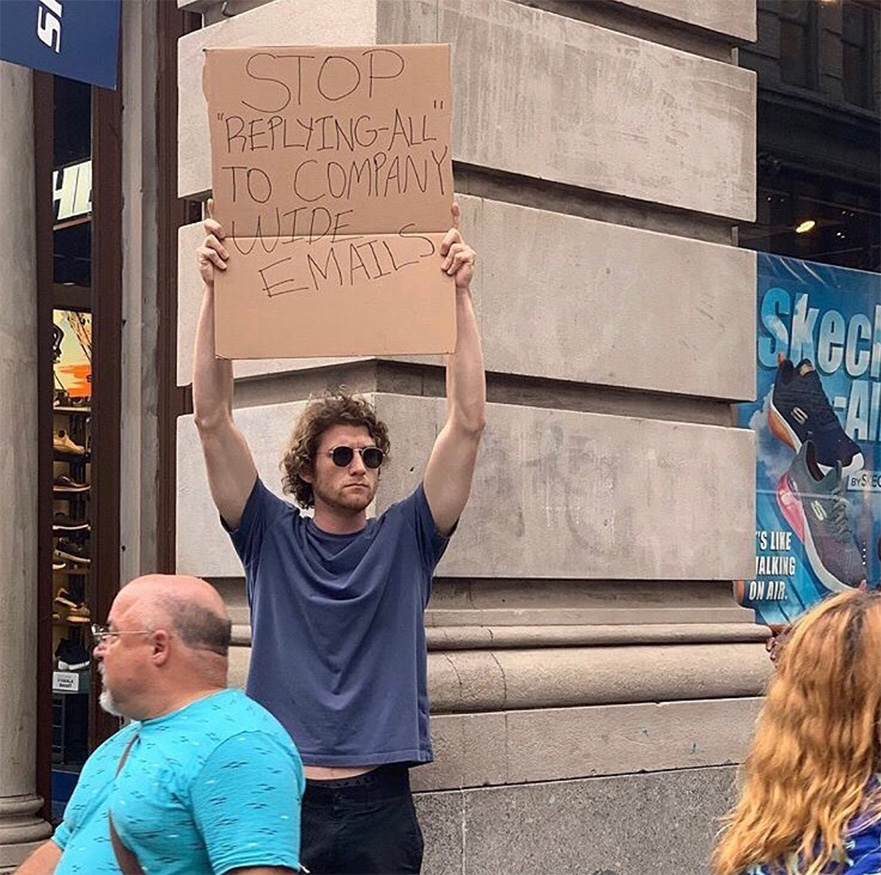 New York's famous "Dude with sign" (@dudewithsign) outside a building. His sign says "Stop 'replying all' to company wide emails". A strong message using few words - less is more.